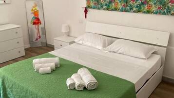 Un dormitorio con una cama, colcha verde, almohadas blancas, una mesita de noche, una lámpara y un cuadro en la pared.