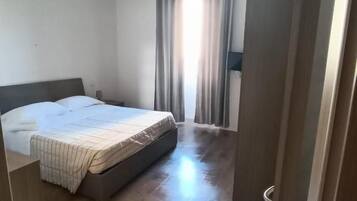 A bedroom with a bed, a chair, a wardrobe, and a window with curtains.