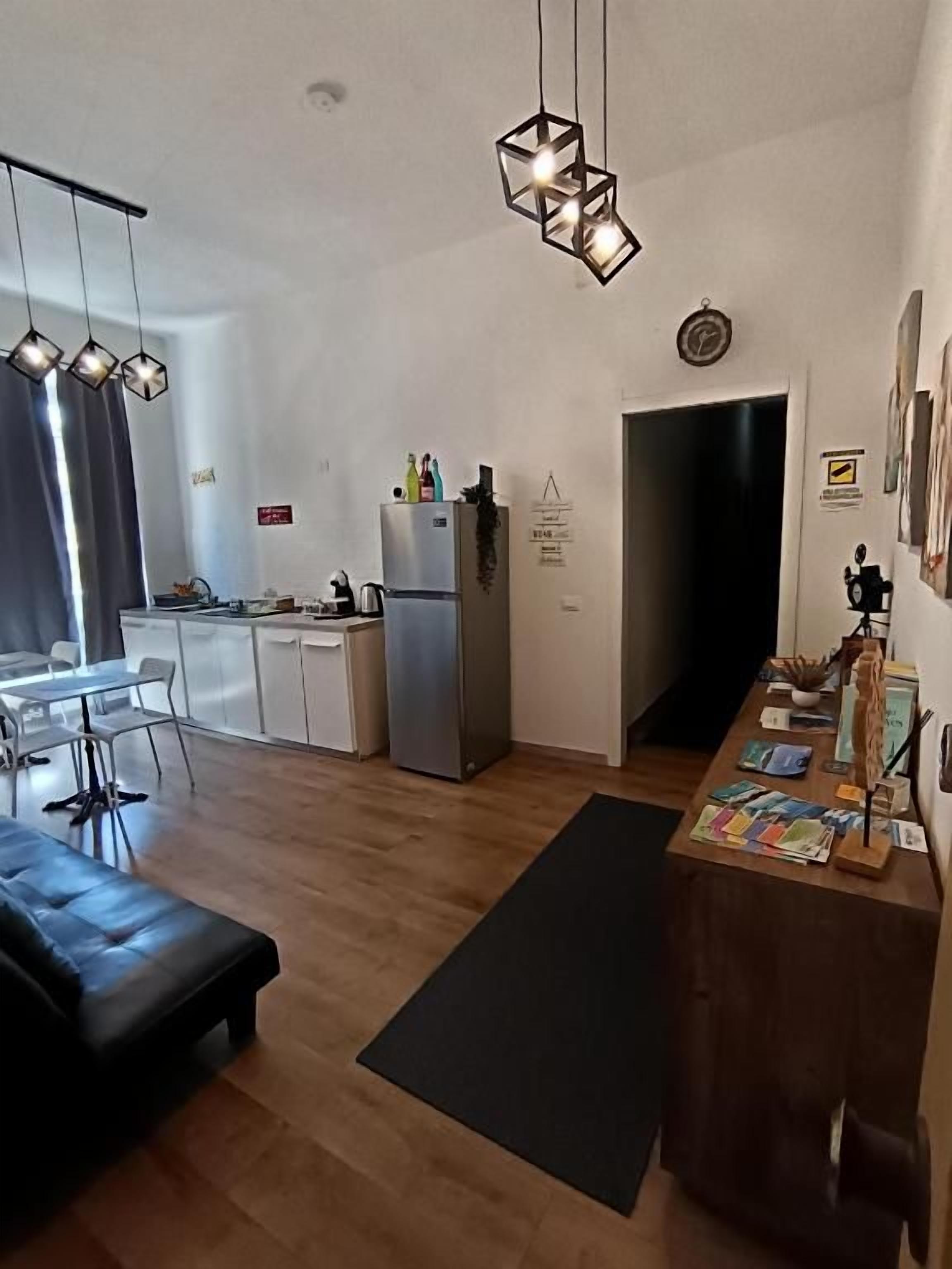 A modern kitchen with a dining area, a black sofa, and a wooden table with books.