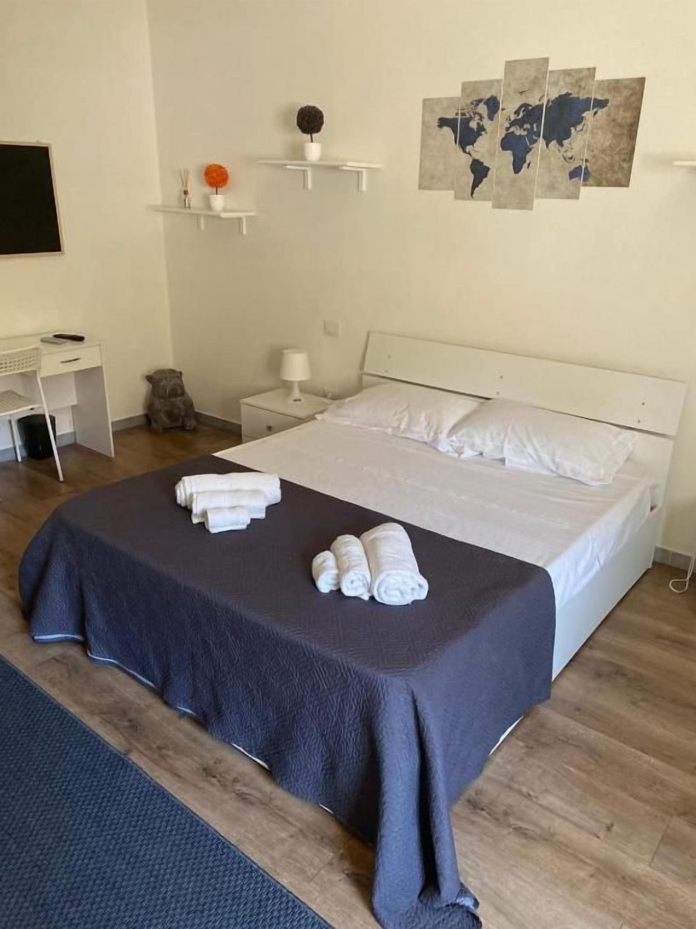 Cama bem arrumada com roupa de cama branca, um espalhadeira azul escura e uma pintura de um mapa mundial na parede.