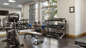 Un gimnasio con equipo cardiovascular, estantes para pesas y una cinta de correr.