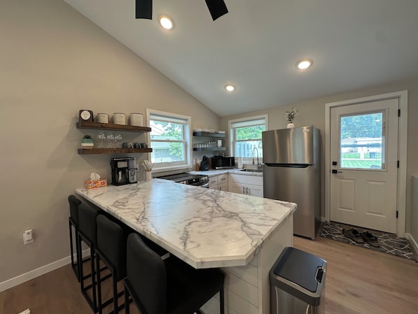 A kitchen with a marble countertop, stainless steel appliances, and a bar area with stools.