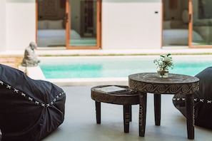 A poolside seating area with a round table and chairs, a statue, and a view of a pool and building. - Villa Pearl — Easy Island Living, Your Way (Ko Samui District)
