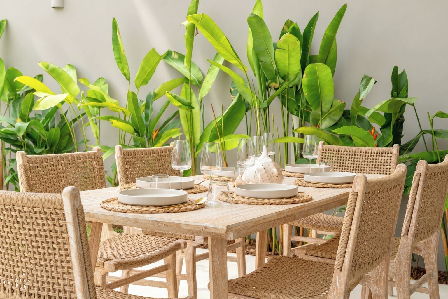 A dining table set with plates, glasses, and a decorative vase, surrounded by wicker chairs.
