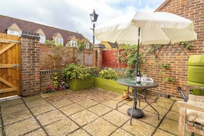 A patio area with a table, chairs, a lamp, and a green planter. - Dutch Cottage Cotswold Stay with Private Parking (Gloucestershire)