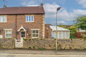 A two-story brick house with a stone wall in front, a white door, and a small porch with a white gate. - Dutch Cottage Cotswold Stay with Private Parking (Gloucestershire)