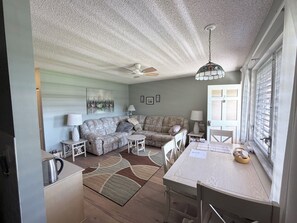 A living room with a sectional sofa, a dining table, a ceiling fan, and a window with blinds. - Charming condo in gorgeous Marco Island perfect for your getaway (Marco Island)