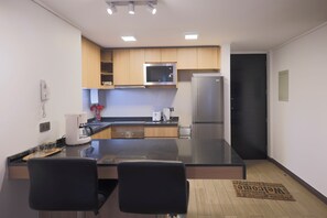 A modern kitchen with a central island, a refrigerator, and a microwave. There are two chairs at the island and a coffee maker on the counter. - Modern 2BR Apartment in Las Condes (Las Condes)