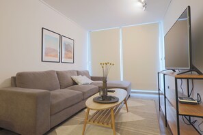A living room with a sofa, a coffee table, a TV stand, and a large window. - Modern 2BR Apartment in Las Condes (Las Condes)