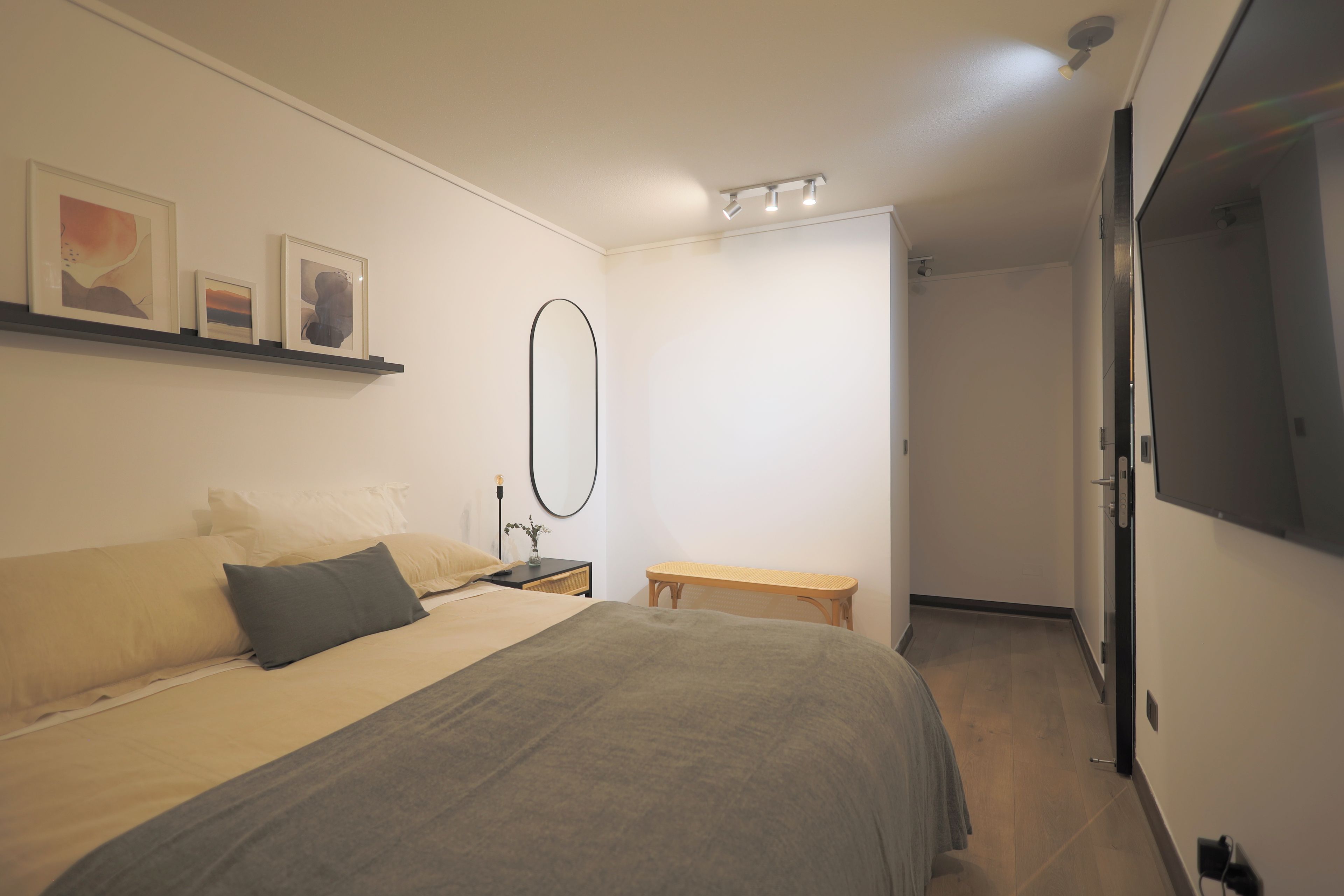 A bedroom with a bed, bedside table, lamp, and a wall-mounted mirror.
