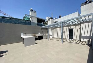 A rooftop terrace with a pergola, a small seating area, and a view of surrounding buildings. - Modern 2BR Apartment in Las Condes (Las Condes)