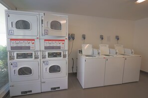 A laundry facility with stacked washing machines and dryers, control panels, and QR codes. - Modern 2BR Apartment in Las Condes (Las Condes)