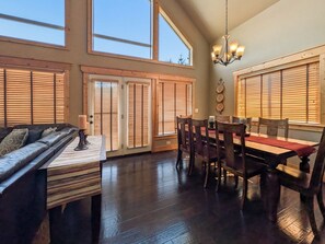 A spacious dining area with a high ceiling, large windows, and a wooden dining table with chairs. - McCall Mountain Escape | Loft, Deck & Ping Pong (McCall)