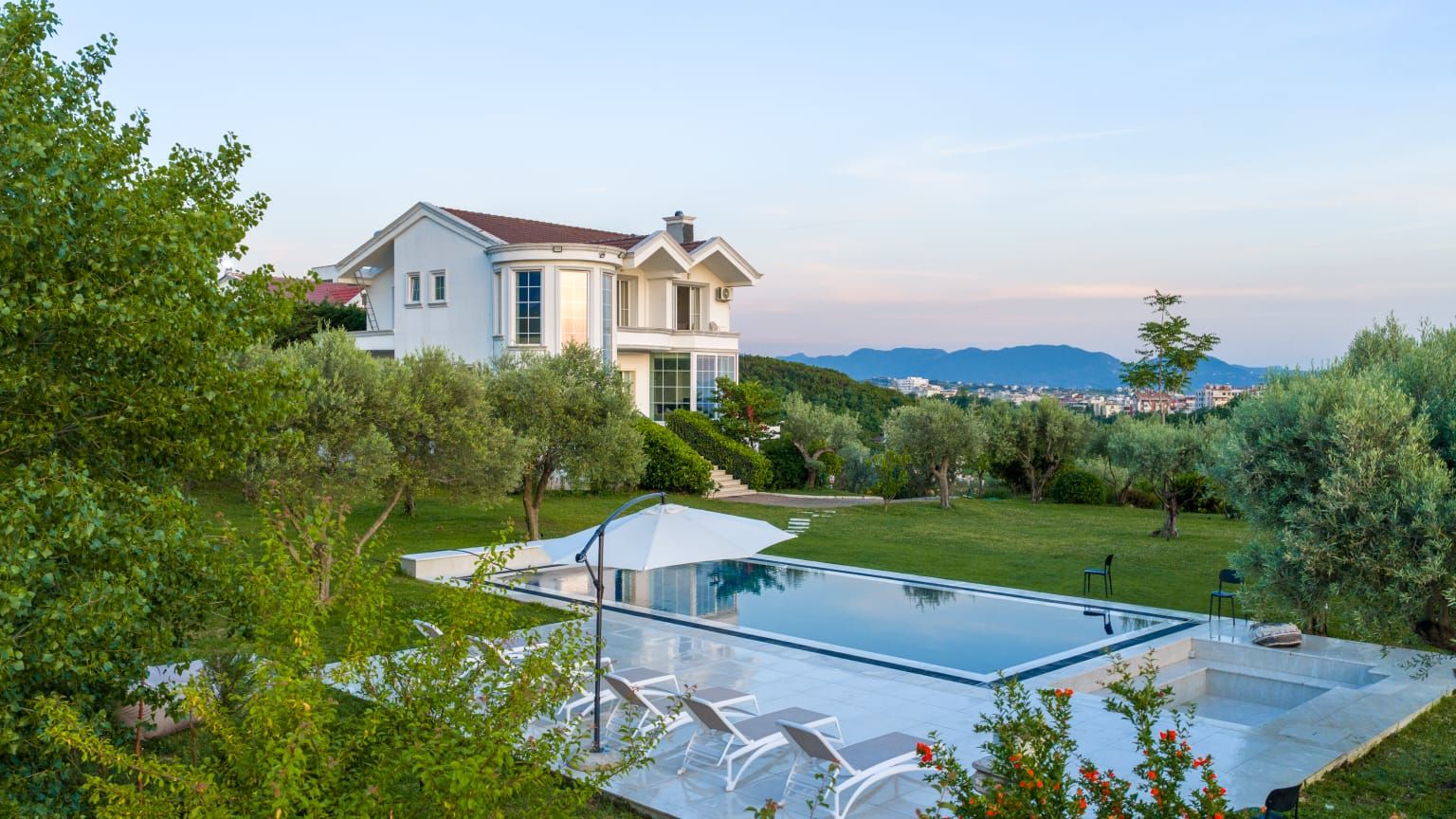 Una casa moderna con piscina, rodeada de exuberante vegetación y vistas a montañas distantes.