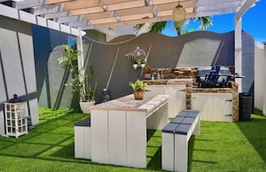 A backyard with a built-in barbecue area, a small seating area, and a potted plant. - Zen Nest • Cozy Studio • 3-Min Drive to Palm Beach (Noord)