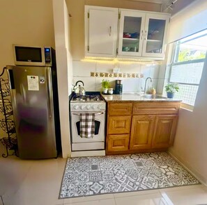 A compact kitchen with a refrigerator, stove, and wooden cabinets. - Zen Nest • Cozy Studio • 3-Min Drive to Palm Beach (Noord)