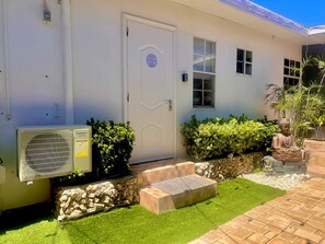 A house with a white exterior, a door with a circular emblem, an air conditioning unit, a small window, and a statue of a seated figure. - Zen Nest • Cozy Studio • 3-Min Drive to Palm Beach (Noord)