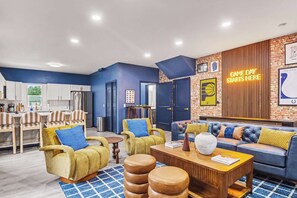 A modern living room with a blue sofa, yellow armchairs, and a coffee table. - Indy Escape | Sauna, Hot Tub, Firepit & Games (South Bend)