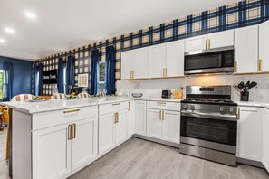 A modern kitchen with white cabinetry, gold handles, a stainless steel range, and a microwave. - Indy Escape | Sauna, Hot Tub, Firepit & Games (South Bend)