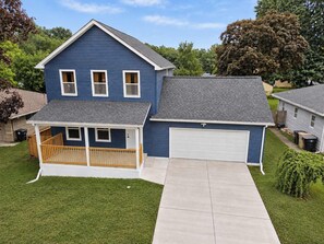 A two-story residential house with a front porch, a garage, and a well-maintained lawn. - Indy Escape | Sauna, Hot Tub, Firepit & Games (South Bend)
