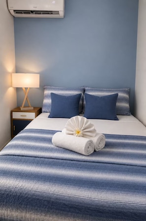 Ein Hotelzimmer mit Bett, Kissen, Nachttisch, Lampe und einem zusammengerollten Handtuch mit einer Blume.