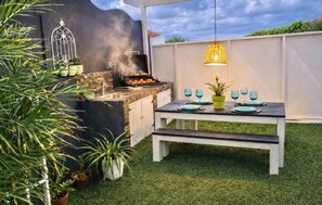An outdoor patio with a grill, a dining table set with blue glassware, and a hanging light fixture. - 2BR/2BA Retreat • King Bed • 3 Min to Palm Beach (Noord)