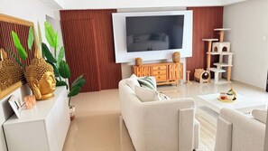 Ein modernes Wohnzimmer mit Flachbildfernseher, einer Couch, einem Couchtisch, einem Kratzbaum und Zimmerpflanzen.