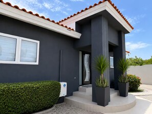 Ein modernes Haus mit dunkler Fassade, einem Ziegeldach und einem gepflegten Vorgarten mit Hecke und Kübelpflanzen.