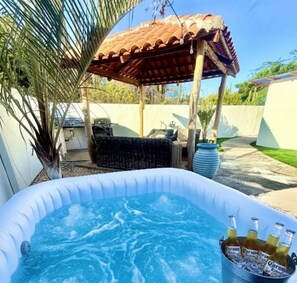 Un bain à remous extérieur, surmonté d’une pergola, entouré de verdure et agrémenté d’un espace patio avec des meubles d’extérieur.