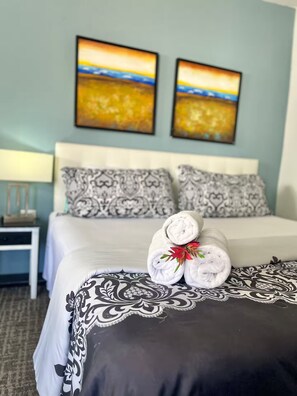 Une chambre d’hôtel avec un lit, deux oreillers, une table de chevet, une lampe et deux tableaux au mur.