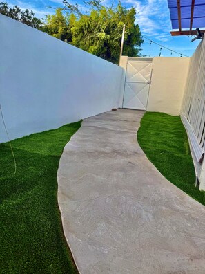 A concrete pathway leading to a gated area with a white wall on one side and a wooden fence on the other. - Romantic King Studio w/ Private Jacuzzi Palm beach (Noord)