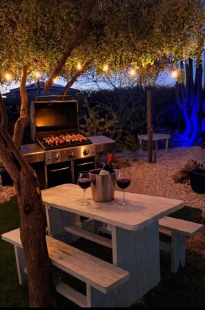 An outdoor barbecue area with a grill, a table with wine glasses, and benches. - Private Patio Retreat • 3 Min to Palm Beach (Noord)