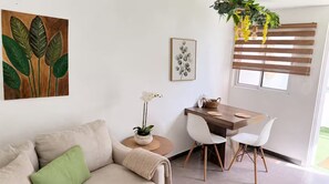 A modern living room with a sofa, a dining table with chairs, a potted plant, and a window with blinds. - Private Patio Retreat • 3 Min to Palm Beach (Noord)