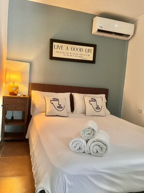 Habitación de hotel con cama, almohadas, lámpara de noche, aire acondicionado de pared y una cita motivacional en la pared.