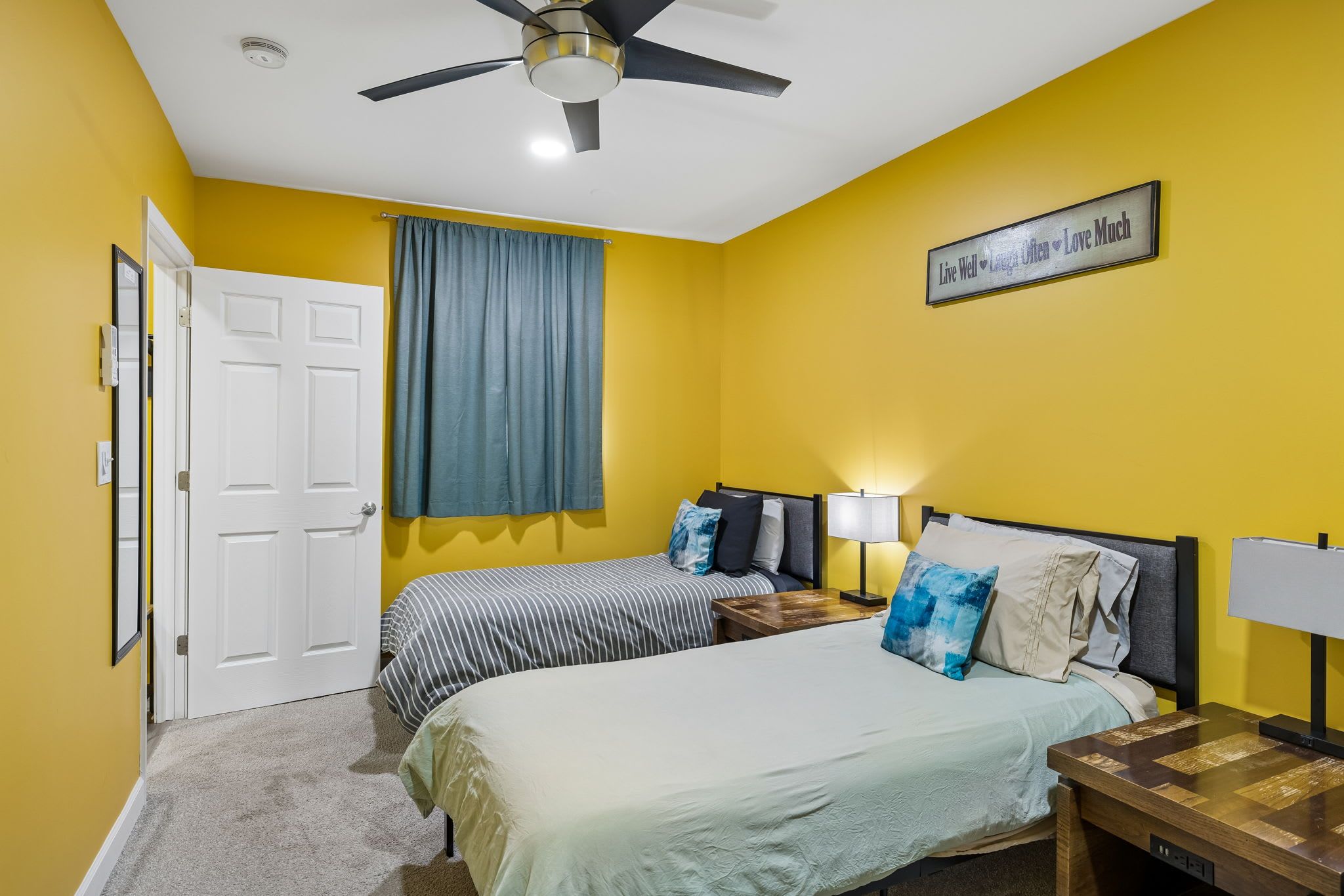 A bedroom with two beds, a ceiling fan, a wall-mounted light, and a motivational quote.