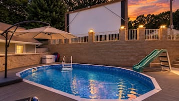 A swimming pool with a slide, a covered seating area, and a view of the sunset.