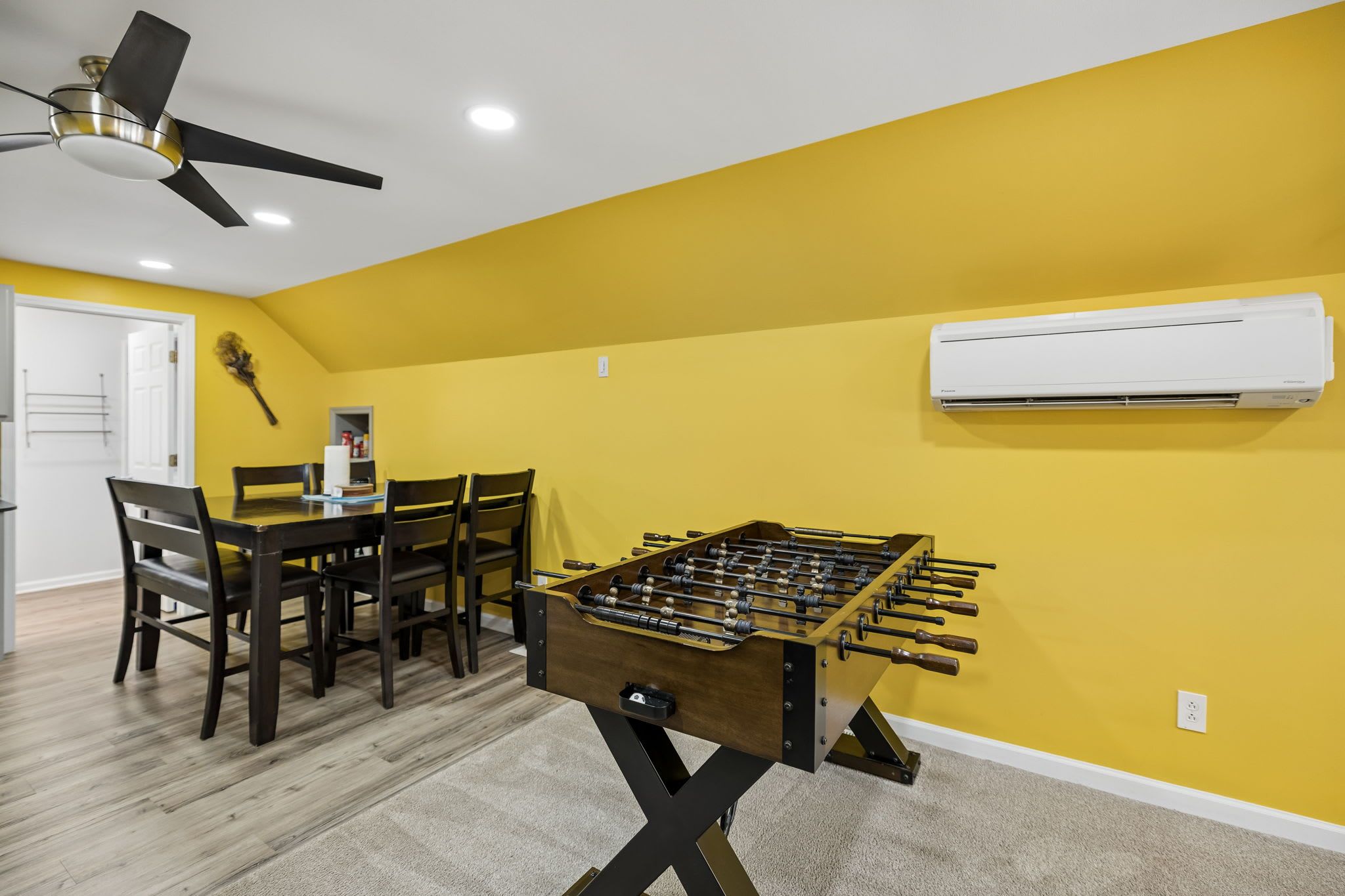 A room with a foosball table, a ceiling fan, and an air conditioning unit.