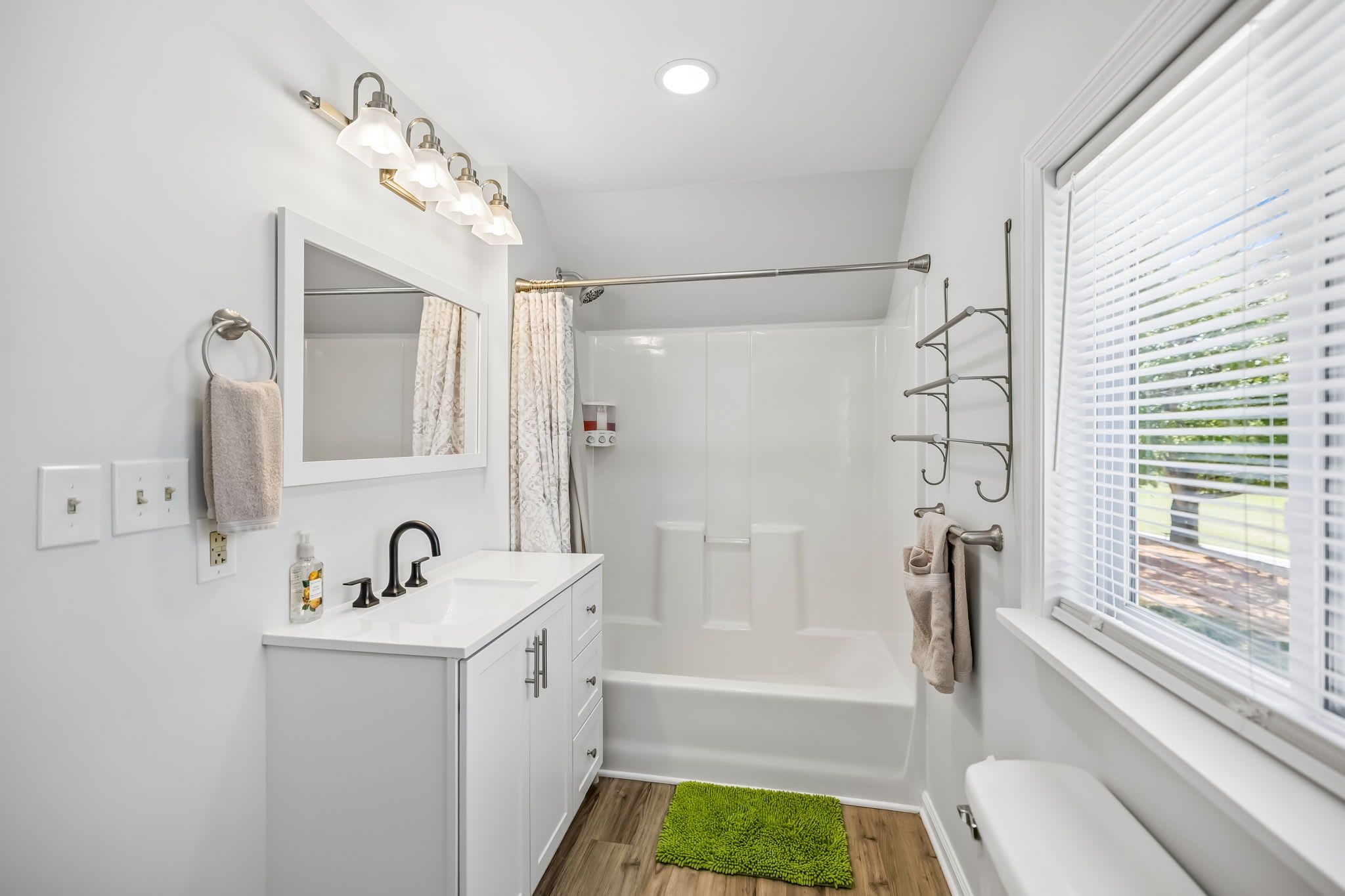 A modern bathroom with a shower, a vanity with a mirror, and a window with blinds.