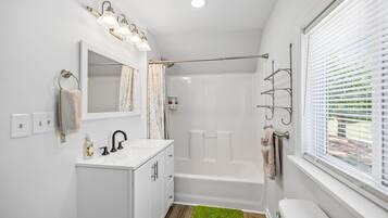A modern bathroom with a shower, a vanity with a mirror, and a window with blinds.