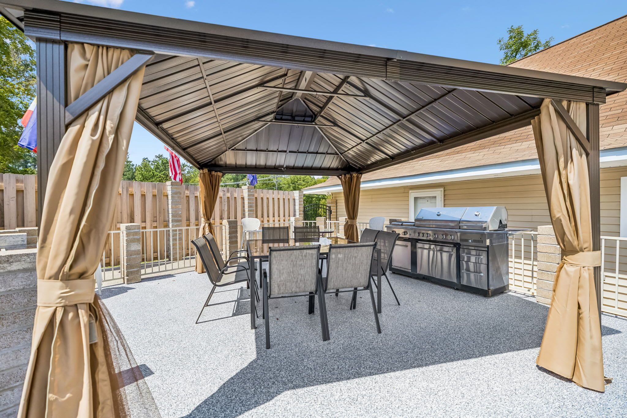 An outdoor patio with a covered grill area, seating, and a view of a house.