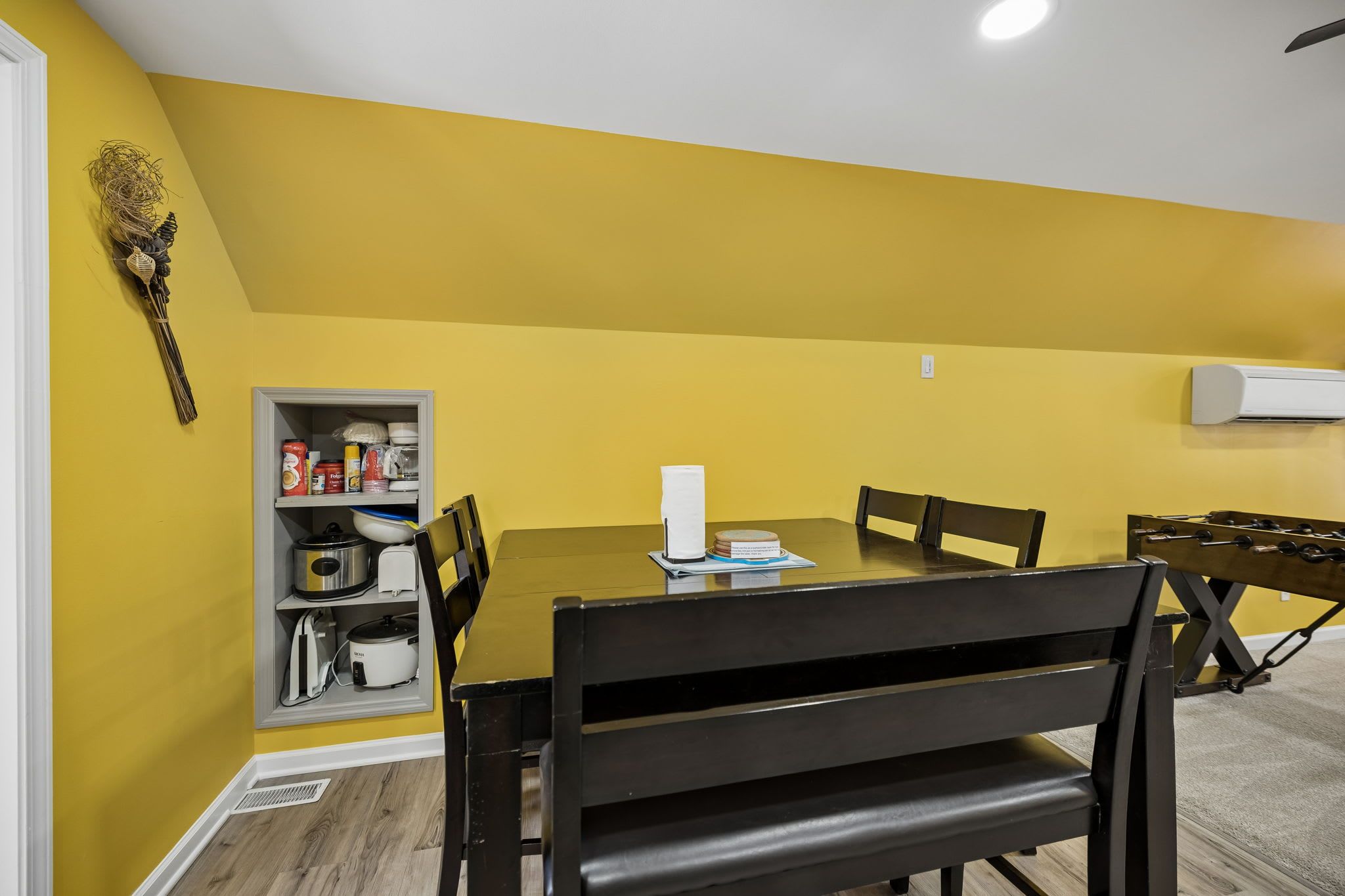 Un comedor con una mesa, sillas y un armario de cocina frente a una pared amarilla.