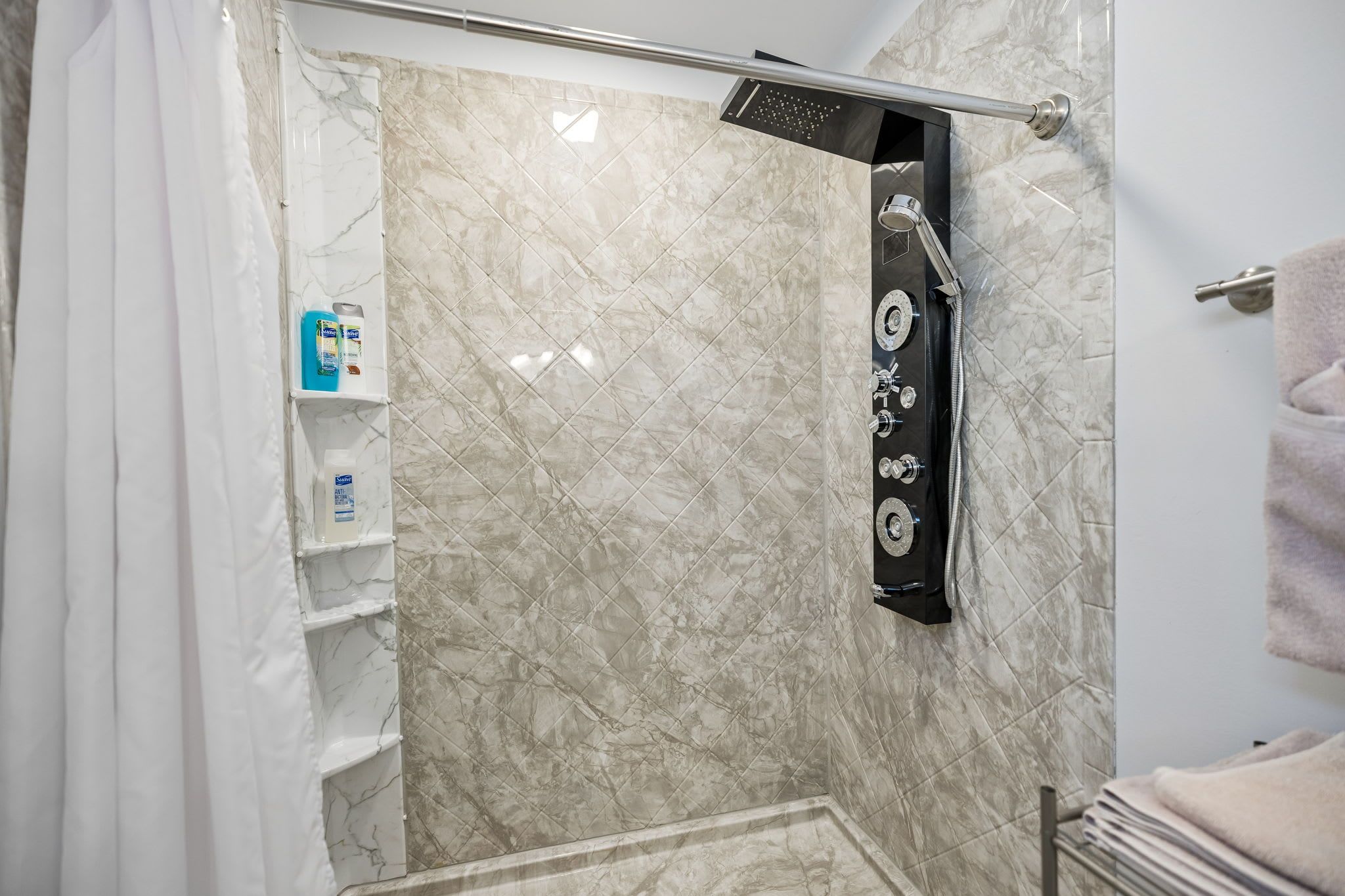 Une salle de bain avec une douche, des carreaux de marbre, un porte-serviettes et des articles de toilette rangés sur une étagère.
