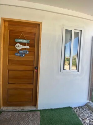 A wooden door with a sign that reads 'HAPPINESS IS A HABIT' and a window with a view of the outdoors. - Private 1BR Retreat • 3 Min to Palm Beach (Noord)