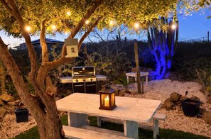 An outdoor patio with a grill, a table, and string lights. - Private 1BR Retreat • 3 Min to Palm Beach (Noord)