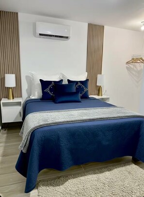 A hotel room with a large bed, a bedside table with a lamp, and a wall-mounted air conditioning unit. - Private 1BR Retreat  • 3 Min to Palm Beach (Noord)