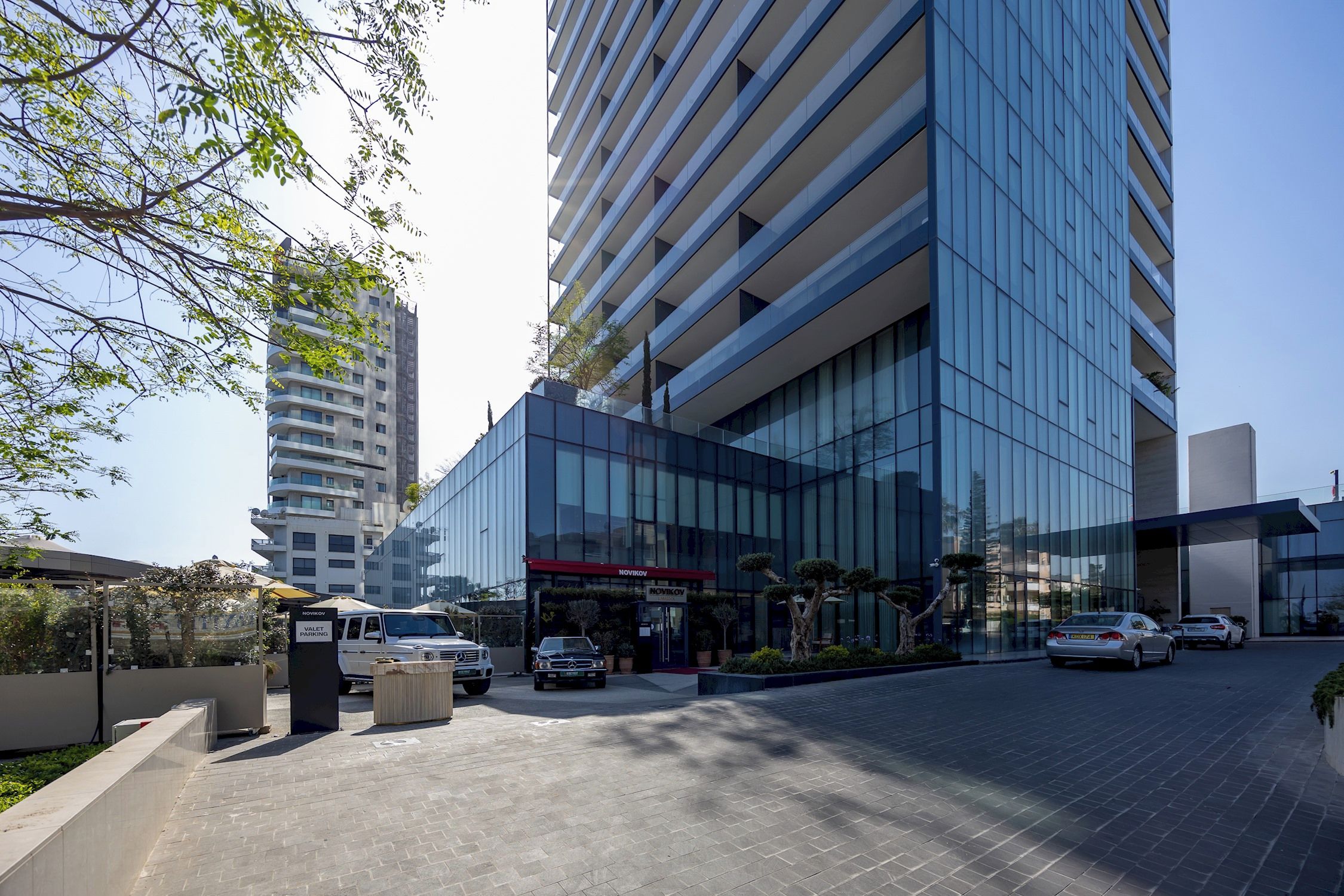 A modern building with a glass facade, a parking area, and a sign for valet parking.