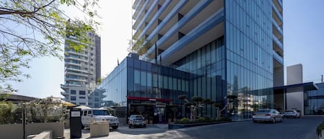 A modern building with a glass facade, a parking area, and a sign for valet parking.