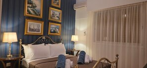 Ein Hotelzimmer mit Bett, zwei Nachttischlampen, einem Fenster mit durchsichtigen Vorhängen und Wandbildern.