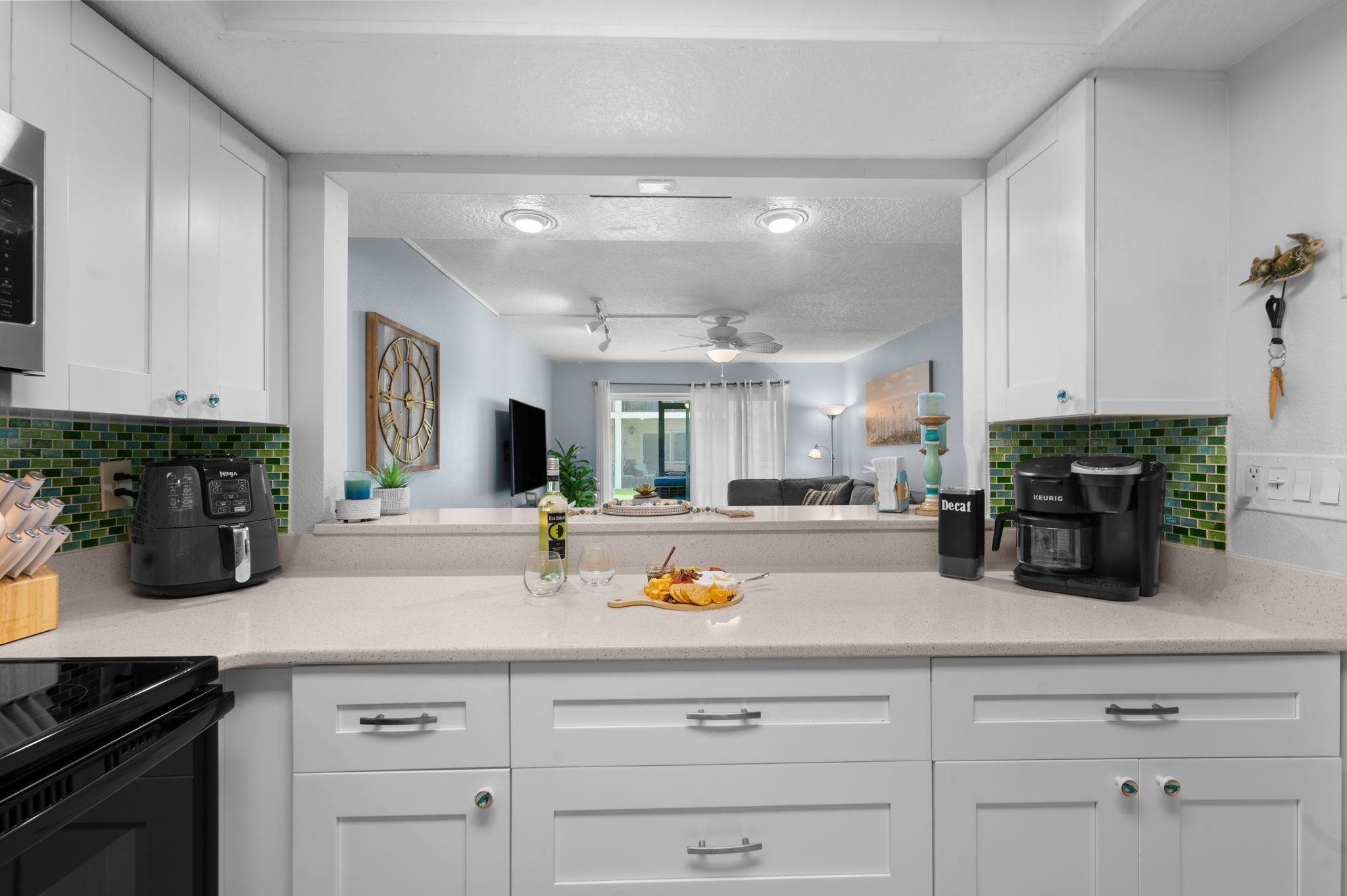 A modern kitchen with white cabinets, a central island, and a dining area visible through an open door.