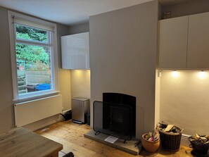 A compact kitchen with a built-in fireplace, a window with a view of greenery, and a small trash bin. - Gorgeous 3-bedroom townhome on Endcliffe Park (Sheffield)